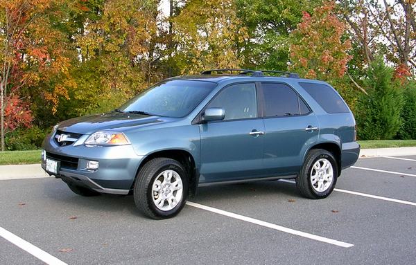 A blue 4-door sport utility vehicle viewed from the front on the driver's side, showing a good view of the front and driver's side of the vehicle while it is parked in a lot in front of a strip of grass and trees