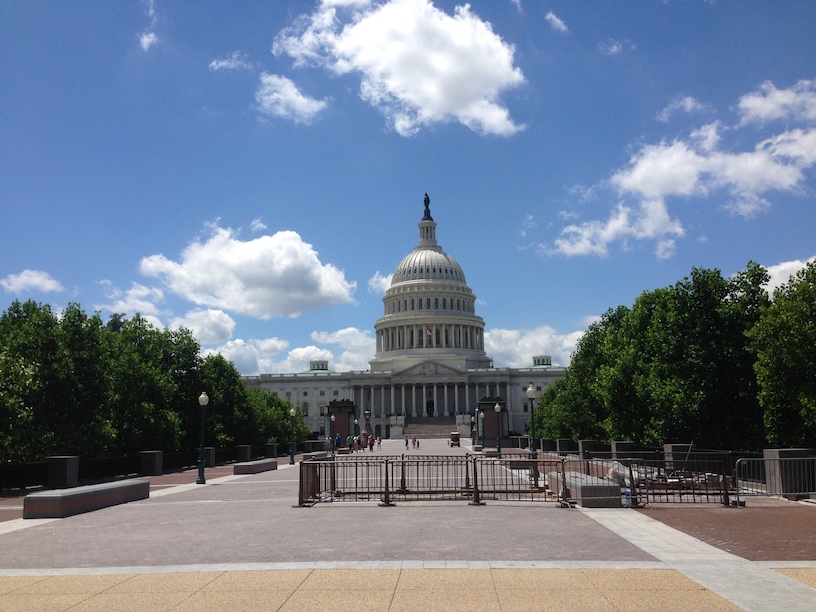 The U.S. Capitol Building viewed from a distance, with a plaza in the foreground and trees on both sides