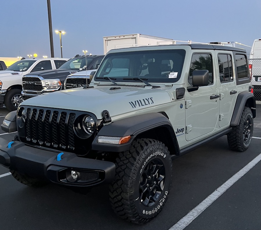 A light green with black trim 4-door sport utility vehicle viewed from the front on the driver's side, showing a good view of the front and driver's side of the vehicle, parked on an asphalt lot with some trucks in the background