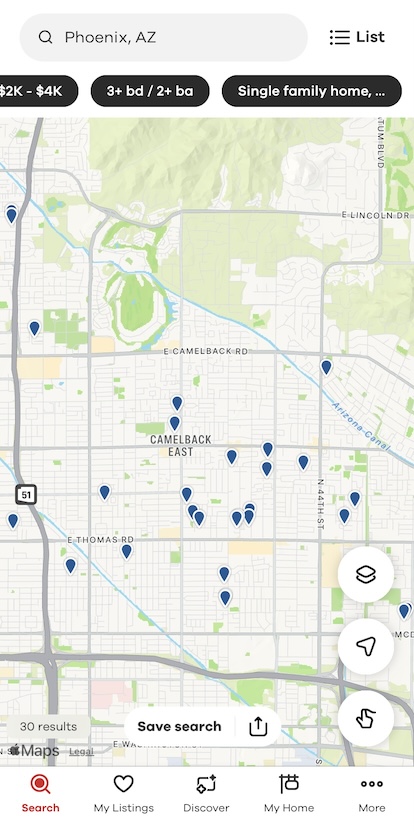 A screenshot from a vertically-oriented smartphone application, most of which consists of a map showing major highways and streets, along with a couple dozen small blue balloon icons sprinked around the map, with a search bar at the top of the screen and navigation buttons at the bottom